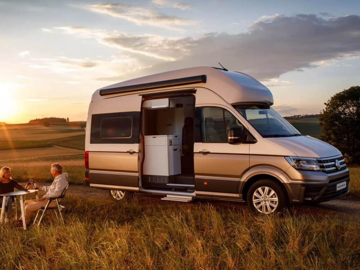 Volkswagen Grand California camper at sunset with two people at a camping table and chairs