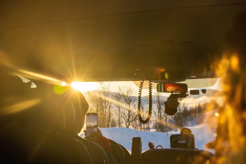 View from a camper cab driving into the low winter sun past snowy fields